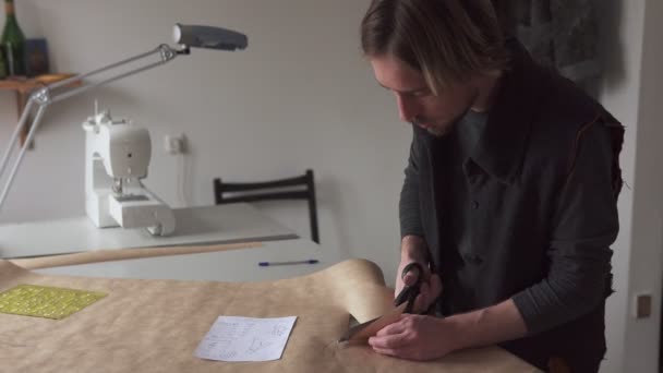 Hombre diseñador corte patrón de ropa de acuerdo a boceto creativo en el lugar de trabajo — Vídeo de stock