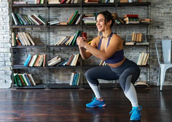 Mulher fazendo agachamento treino e sorrindo durante o treinamento de fitness em casa Imagens De Bancos De Imagens