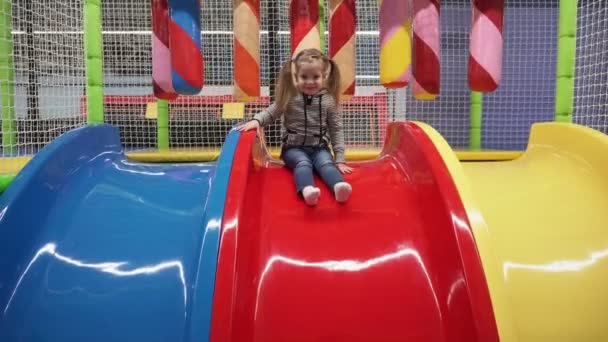 Menina feliz movendo para baixo slide no parque infantil no centro das crianças — Vídeo de Stock