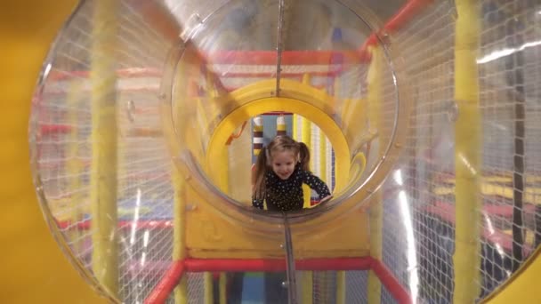 Petite fille rampant à travers le tunnel sur les enfants terrain de jeu à l'intérieur — Video