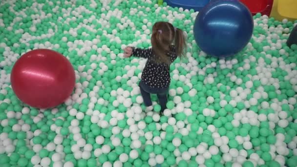 Μικρό κορίτσι με τα πόδια σε μικρά μπαλάκια στο παιδικό παιχνίδι κέντρο — Αρχείο Βίντεο