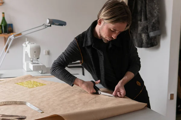 Diseñador de moda masculino con tijeras corta patrón de ropa de papel en taller Fotos de stock