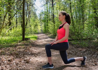 Fitness kadın yaz ormanda çalıştırmadan önce ön lunge yapıyor