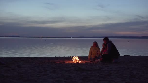 Familia de viajeros que se relajan junto al fuego en la playa — Vídeo de stock