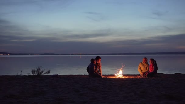 子供を持つ旅行者の家族は、海で夜のキャンプファイヤーの周りに休息 — ストック動画