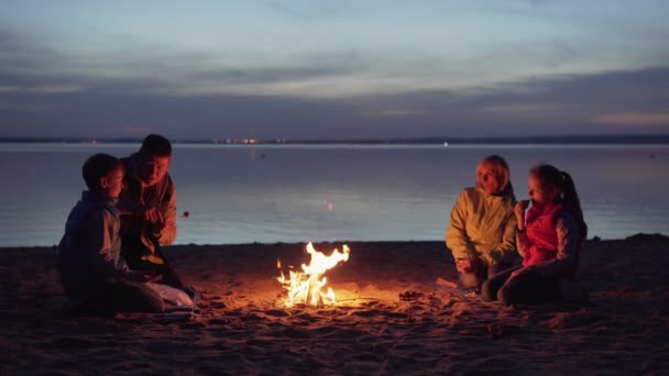 Cena familiar junto a la fogata en la playa por la noche — Vídeo de stock