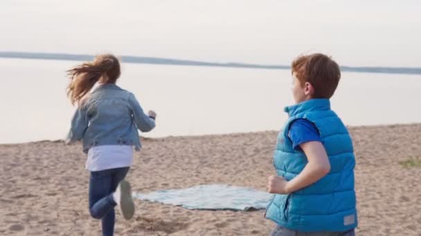 Двоє дітей біжать піщаним пляжем до моря — стокове відео