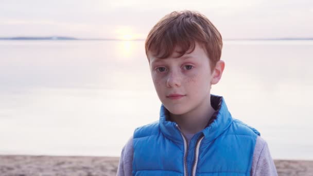 Ładny rudowłosy chłopak z piegi przez morze w zachód słońca — Wideo stockowe