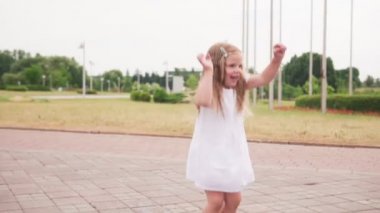 Şehir parkında beyaz elbiseli su birikintisi içinde atlayan küçük mutlu yalınayak kız