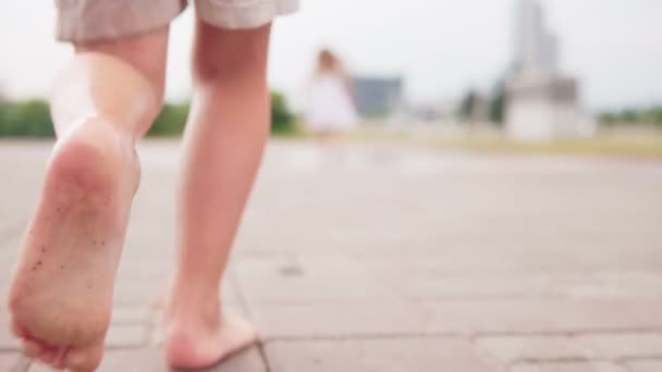 Маленький босоногий мальчик бежит в лужу на городской улице — стоковое видео