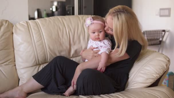 Mother hugs and kisses her adorable baby on sofa — Stock Video