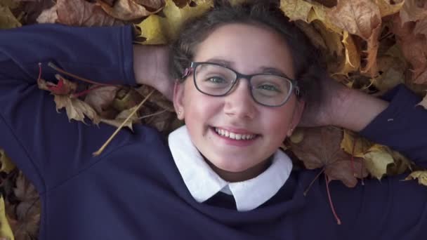 Heureuse écolière se trouve sur les feuilles d'automne et souriant — Video