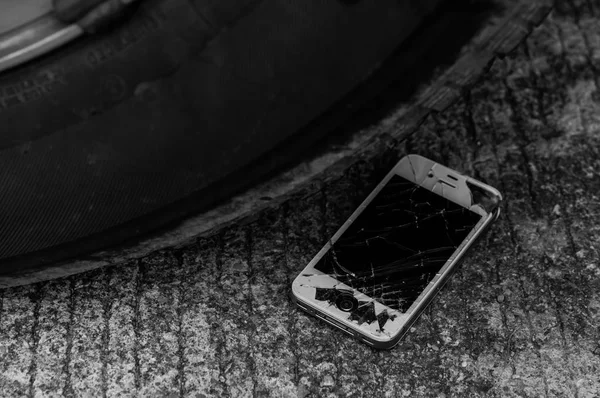 crashed smartphone under car tire on asphalt