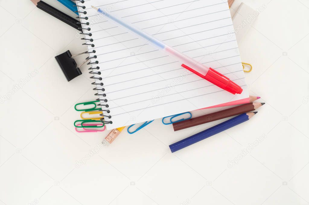 Notebook with pen lying on colorful school supplies on white background 
