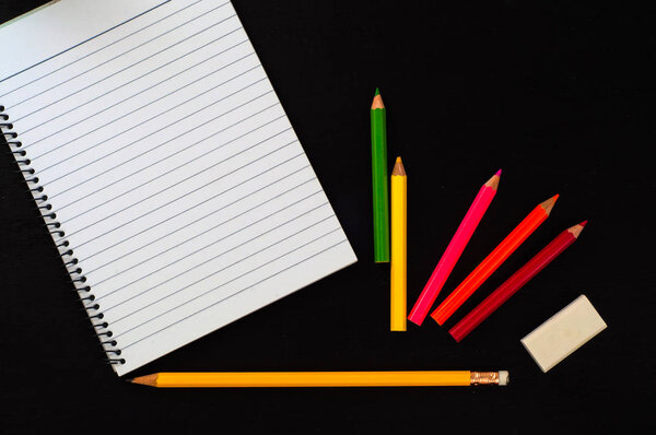 empty notebook with colorful pencils on black background 