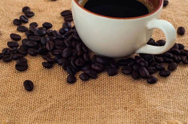 close up of cup with coffee and black beans on sackcloth background