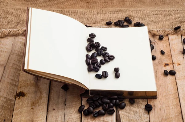 Verstreute Schwarze Kaffeebohnen Und Geöffnetes Notizbuch Mit Leeren Seiten — Stockfoto