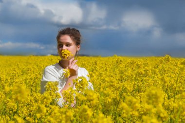 Yazın kolza tohumu tarlasında esmer bir kız, mavi gökyüzü arka planına bakıyor. Mutlu güzel genç kadın neşe ve mutluluk dolu kolza tohumu tarlasının kokusundan hoşlanıyor. Özgürlük kavramı 
