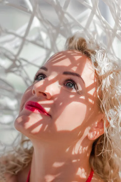 Tek başına açık hava aktiviteleri. Modern bir hamakta, kırmızı mayo giymiş sarışın bir kadının portresi. Otelin çatısında beyaz bir hamakta oturuyor. Orta yaşlı, fit bir kadın. Tatil, seyahat ve tatil kavramı