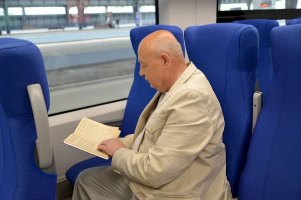 The elderly man reads the book in the electric train car