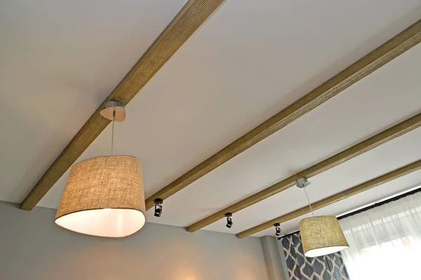 The combined lighting - ceiling chandeliers and laid on lamps on the wooden beams fixed on a ceiling
