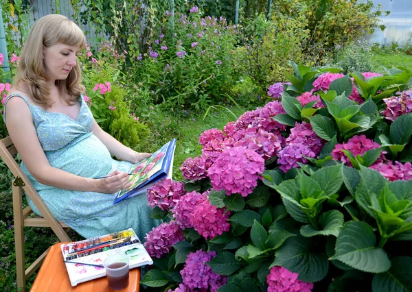 怀孕的女艺术家用水彩画画在花园里开花的绣球花 — 图库照片