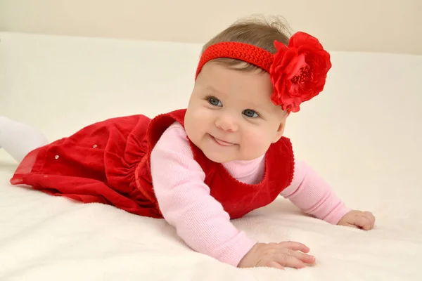 The cheerful six-months girl with a red flower on the head lies on a stomach