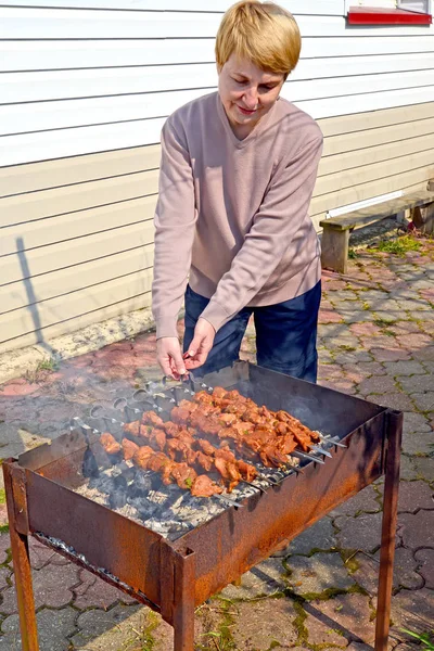 Kobieta średnio lat frytki Shish Kebab o domu wiejskim — Zdjęcie stockowe