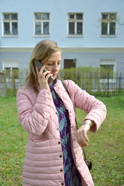 Молодая женщина говорит по мобильному телефону и смотрит на часы — стоковое фото