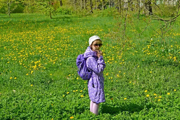 The seven-year-old girl costs among the blossoming dandelions in the park. Spring — Stock Photo, Image