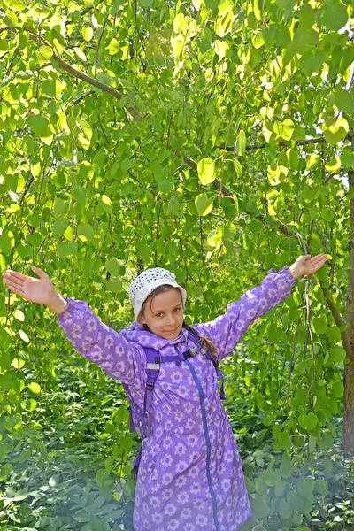A menina custa com as mãos levantadas contra o fundo de uma árvore no parque — Fotografia de Stock