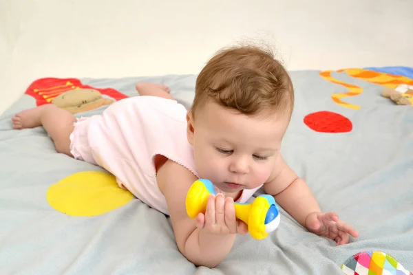 Het kleine kind kijkt naar een rammelaar, liggend op een maag — Stockfoto