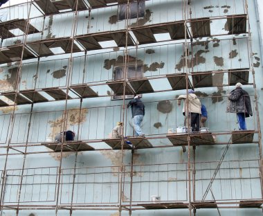 Bir kadın inşaat ekibi çok katlı bir konut un ön cephesini onarıyor.