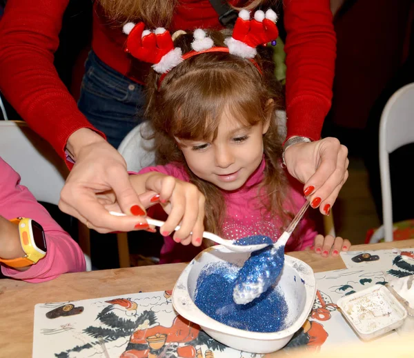 Das Mädchen bestreut das Baumspielzeug mit Glitzer. Meisterkurs für Kinder in der Werkstatt — Stockfoto