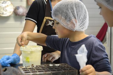 Kaliningrad, Rusya-27 Eylül 2019: Bir çocuk kalıplara dökülmek için beyaz çikolata kütlesi alır. Belgostar çikolata fabrikasına çocuk gezisi.