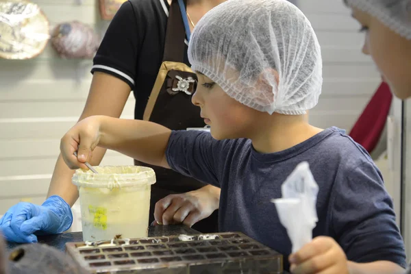 Kaliningrad, Russland 27. September 2019: Ein Junge nimmt eine weiße Schokoladenmasse, um sie in Formen zu gießen. Kinderausflug in die Schokoladenfabrik Belgostar — Stockfoto