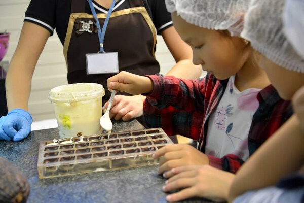KALININGRAD, RUSSIA-SEPTEMBER 27, 2019: a Child pours white chocolate mass into molds. Children's excursion to the belgostar chocolate factory