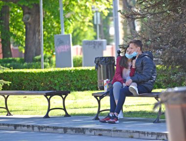 KALININGRAD, RUSSIA - 31 Mayıs 2020: Koruyucu maske takan genç bir çift meydanda bir bankta oturuyor. COVID-19 koronavirüs salgını
