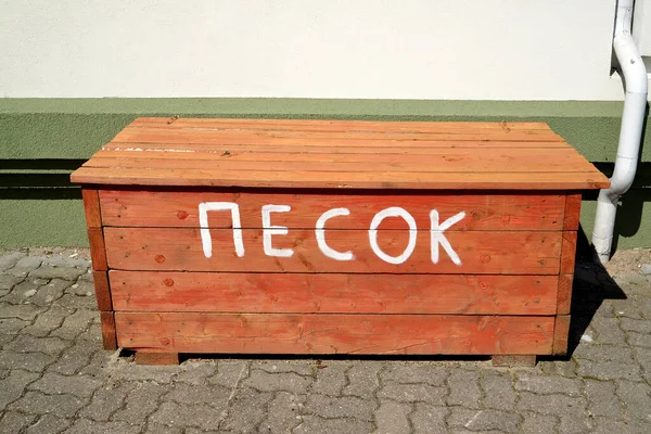 A red fire box with sand stands near the wall of the building. Russian text - sand