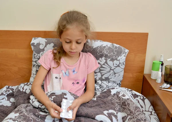 病気の少女はベッドに横たわっている間薬のパッケージを保持しています 自己治療 — ストック写真