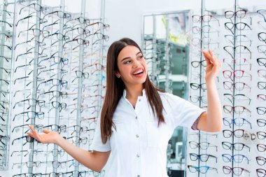 Göz hastalıkları Kliniği çekici genç kadın doktor. Doktor göz doktoruna raflar farklı gözlük ile yakın duruyor.