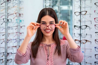 Health care, eyesight and vision concept - happy woman choosing glasses at optics store clipart
