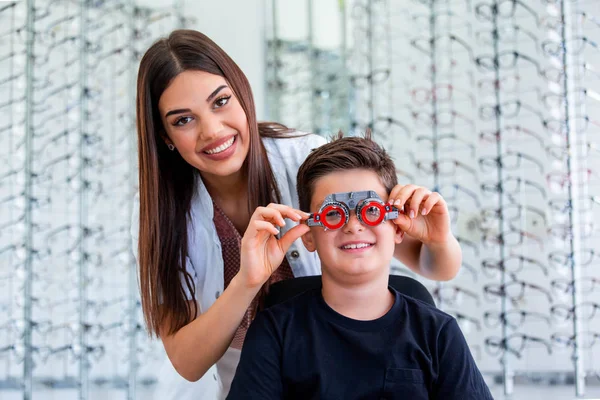 Atraktivní oftalmolog, který zkoumá chlapce s optometristickým zkušebním rámcem. Dětský pacient, který kontroluje vidění na oftalmologické klinice — Stock fotografie