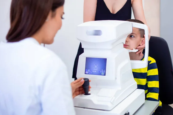 Oculista femenina usando la máquina para comprobar la vista en la clínica. Niño mirando el equipo y el médico examinando la pupila ocular en la tienda óptica. Concepto de cuidado ocular y salud . —  Fotos de Stock