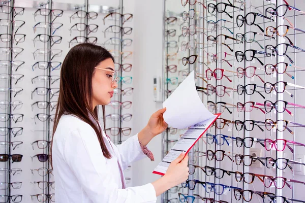 Aantrekkelijke vrouwelijke oogarts schrijven gegevens naar een klembord, werkend in een optische winkel. Gezondheidszorg en geneeskunde concept — Stockfoto