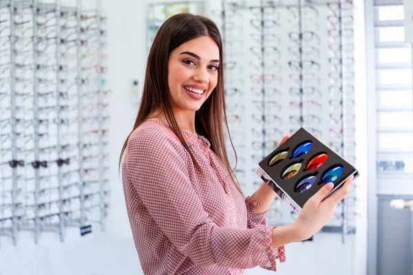 Atractiva doctora joven en clínica oftalmológica que muestra diferentes lentes polarizadas —  Fotos de Stock