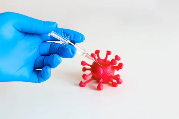 Person holds syringe with vaccine and gives an injection to a red corona virus on the white background. Theme of health care, medical treatment and disease prevention