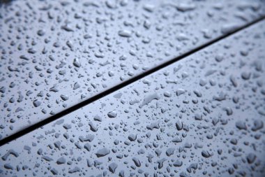 Metalik araba yüzeyinde su damlaları birikmiş.