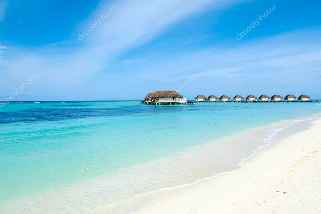 The beautiful landscape of the deserted Indian Ocean sandy beach, shaded by palm trees and tropical plants and over water villas