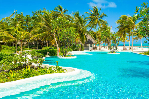 Lhaviyani Atoll, Maldives - 13 July 2018: Pool area on the shores of the Indian Ocean with sunbeds and umbrellas in the shade of the palm trees